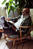 Man with beard reading book in armchair