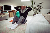 Mature man with beard doing sit-ups on bedroom floor