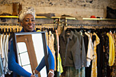 Confident senior female shop owner with mirror in boutique