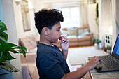 Boy eating strawberries at laptop at home