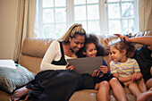 Mother and daughters using tablet on living room sofa