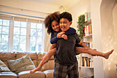 Happy brother piggybacking sister in living room