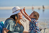 Son lifting mother's hat on beach