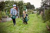 Brothers carrying watering cans on allotment