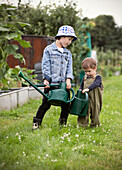 Brothers carrying watering cans in garden grass
