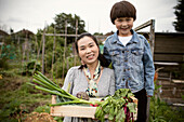 Happy mother and son with harvested vegetables in garden