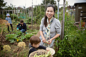 Happy mother and son harvesting vegetables in garden