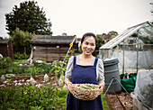 Smiling woman with basket of harvested vegetables in garden