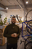 Smiling businessman with coffee next to bikes in office
