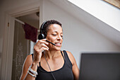 Mature woman in headset working from home at laptop