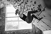 Young woman hanging from climbing wall
