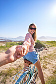 Happy woman riding bicycle holding hand on sunny beach path