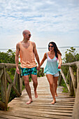 Happy couple holding hands and walking on beach boardwalk