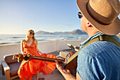 Couple playing guitar and dancing on patio with ocean view