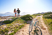 Couple standing on sunny beach with bicycle