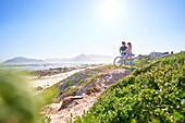 Couple with bicycle on sunny, sandy ocean beach path