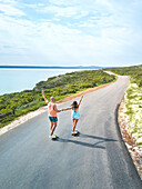 Carefree couple riding skateboards on sunny ocean road