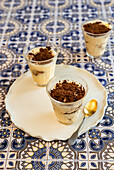 Tiramisu served as individual servings in glasses on a ceramic plate and tiled surface
