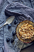 Geröstete Mandeln im Schälchen daneben Blaubeeren und Löffel mit Joghurt