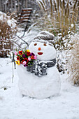 A snowman with a bouquet of tulips in a garden
