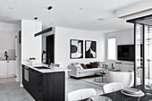 Wohnzimmer mit grauem Sofa und abstrakten Kunstwerken, danebe offene Küche mit kleiner Waschküche im Hintergrund