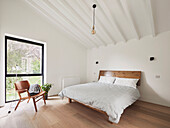 Holzbett und Stuhl im schlichten Schlafzimmer mit hoher Decke