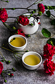 Asian green tea with red mini roses on concrete background