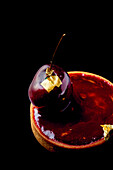 Rotwein-Kirsch-Törtchen mit Blattgold vor schwarzem Hintergrund