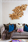 Sofa mit Kissen, darüber vergoldete Blätter-Installation