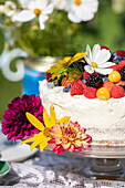 Festliche Torte dekoriert mit Früchten und Blüten auf Tisch im Freien