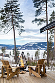 Holzstühle und Feuerschale auf Terrasse mit Blick auf schneebedeckte Landschaft, Brøttum in der Region Ringsaker, Innlandet, nähe Lillehammer, Norwegen