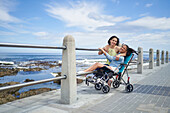 Happy mother and disabled daughter in pushchair at beach