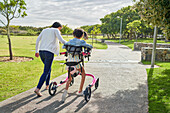 Mother and disabled daughter with rollator walking in park