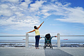 Mother and daughter in pushchair stretching arms at ocean