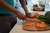 Man slicing fresh carrots with knife at cutting board