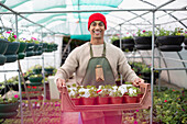 Happy male garden shop owner with tray of potted flowers