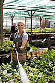 Happy female garden shop owner watering plants with hose