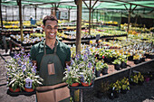 Happy male garden shop owner with trays of potted flowers