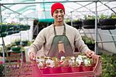 Smiling male plant nursery worker with potted flowers
