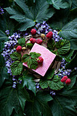 Natural raspberry soap surrounded by flowers, leaves, and raspberries