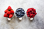 Strawberries, blueberries, and raspberries in small bowls on a concrete base