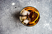 Alcohol cocktail with coke in the glass with orange and ice on grey concrete background