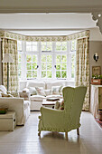 Green and white checked wing chair and sofa in the living room, flowered curtains at the bay window