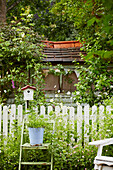 Bepflanzter Eimer auf Gartenstuhl vor Zaun mit Vogelhaus
