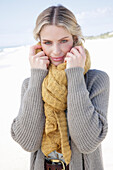 Young blonde woman with a yellow scarf in a grey cardigan on a beach