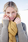 Young blond woman with yellow scarf in grey cardigan on beach