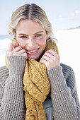 Junge blonde Frau mit gelbem Schal in grauer Strickjacke am Strand