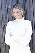 Young blond woman in white knitted jumper in front of board wall