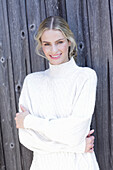 Young blond woman in white knitted jumper in front of board wall