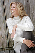 A mature blonde woman wearing a white knitted jumper and grey leggings